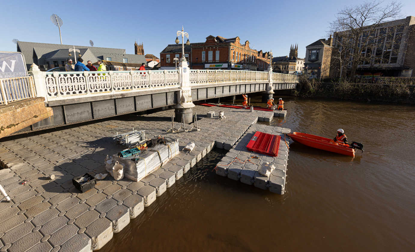 Large modular floating pontoon platform installed beneath city bridge with safety boat support for inspection and maintenance works