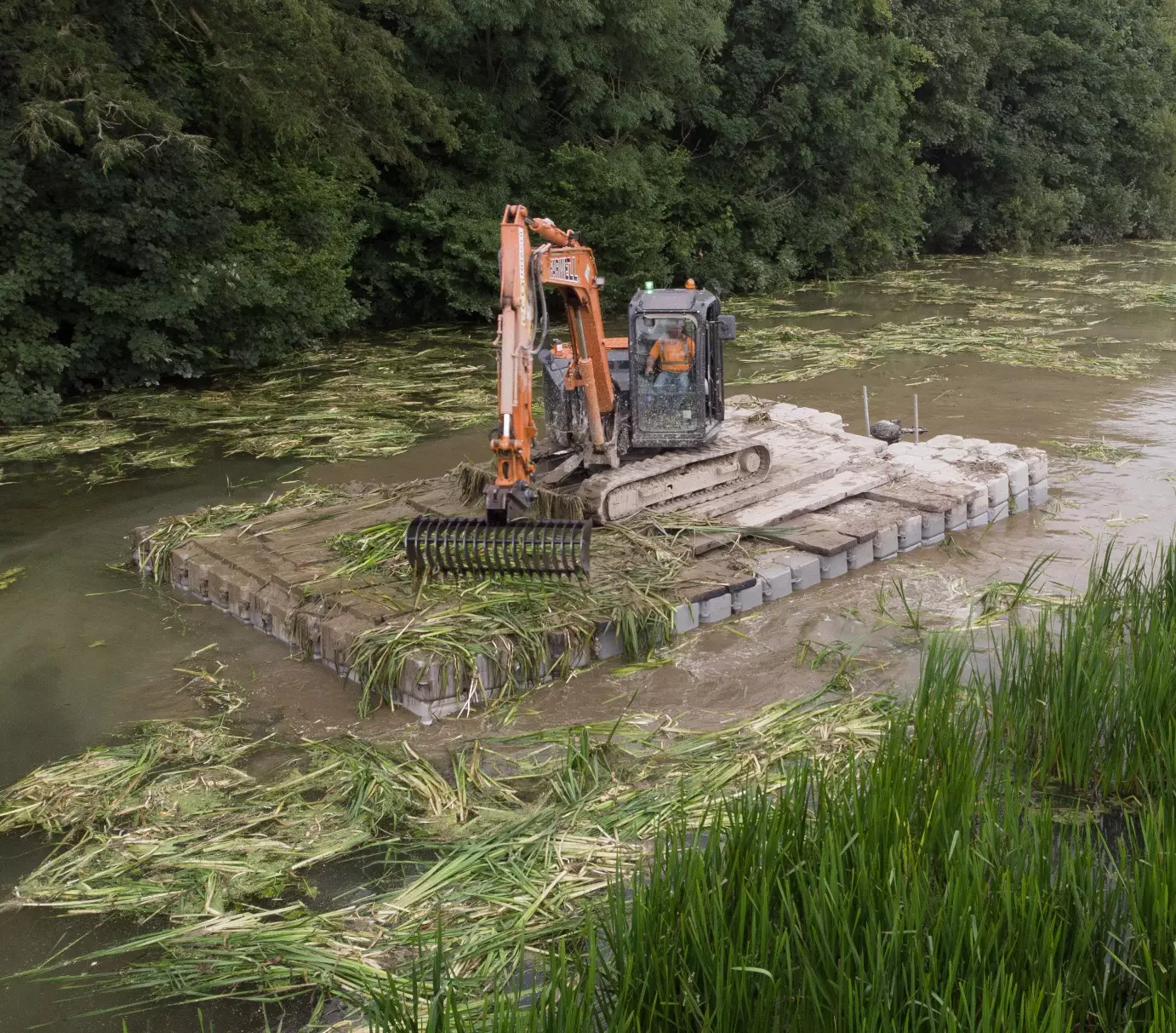 Excavator operating from a modular floating pontoon platform for river vegetation removal and in-water maintenance works