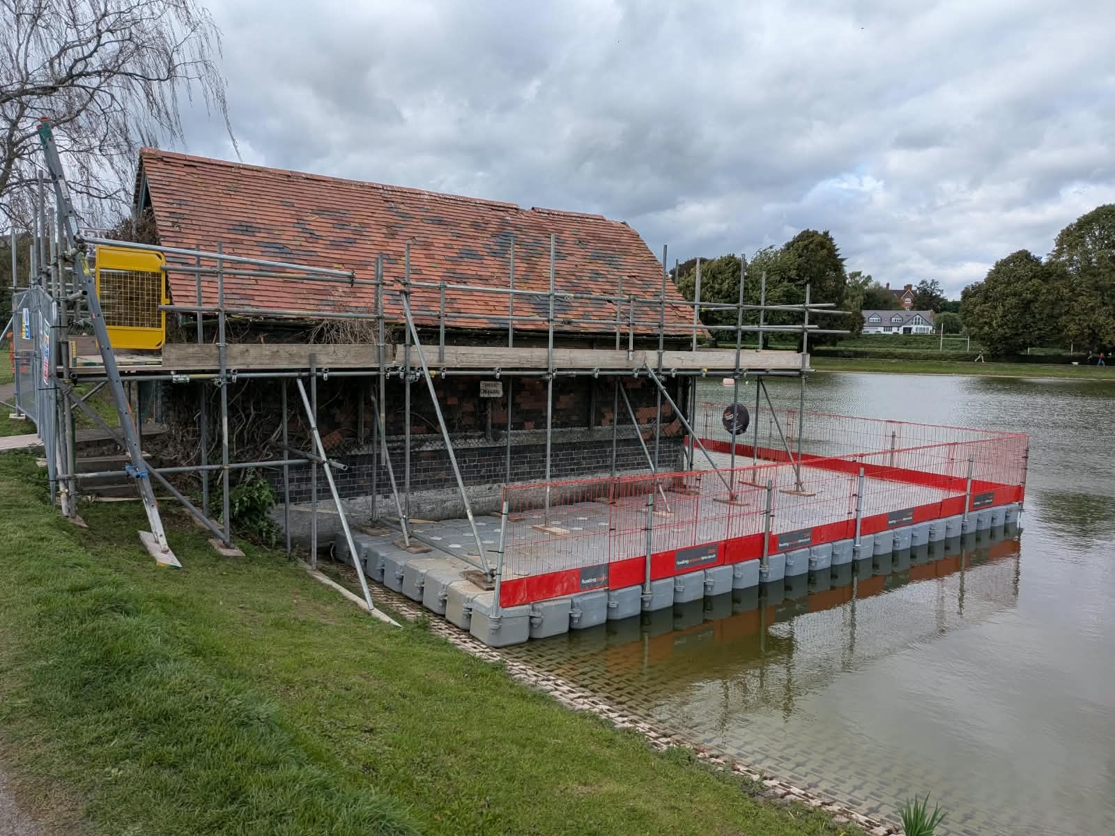 Modular floating pontoon hire platform providing safe, stable water access for scaffolding and building restoration work alongside a lakeside property.