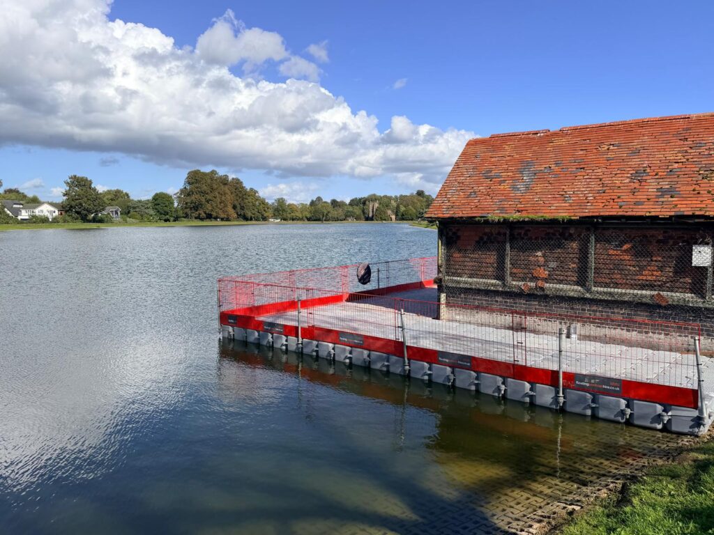Modular floating pontoon with red edge protection installed alongside a brick lakeside building, providing a stable access platform over the water.