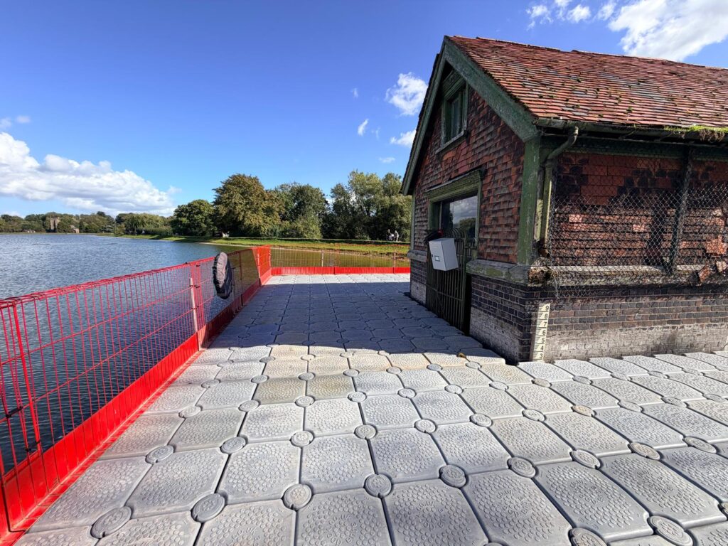 Modular floating pontoon platform installed around a lakeside building, with red edge protection providing safe access and a large working area over the water.